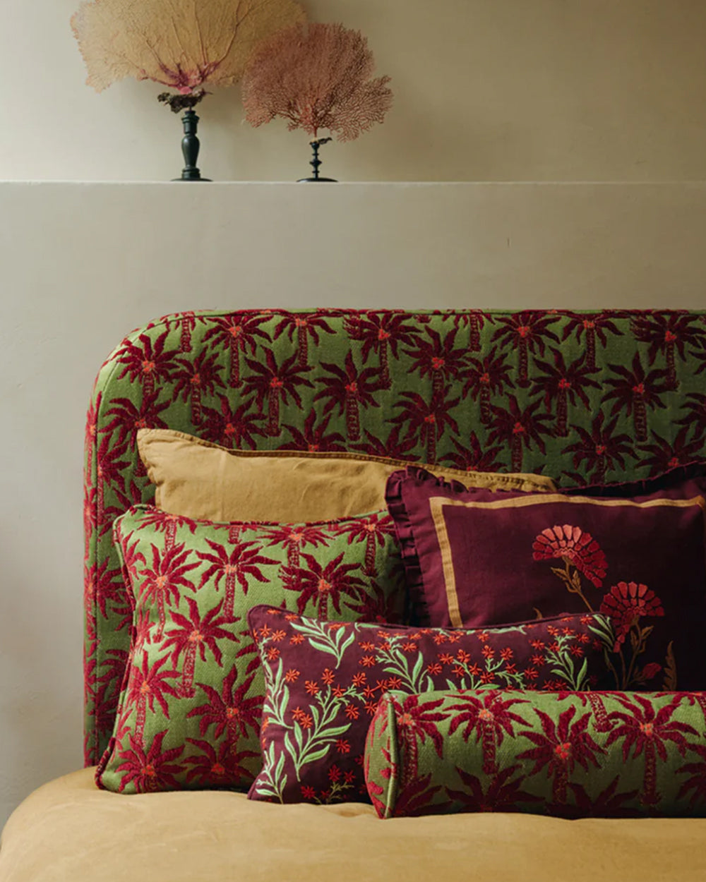 A bed filled with luxurious pillows in green shades with palm tree patterns