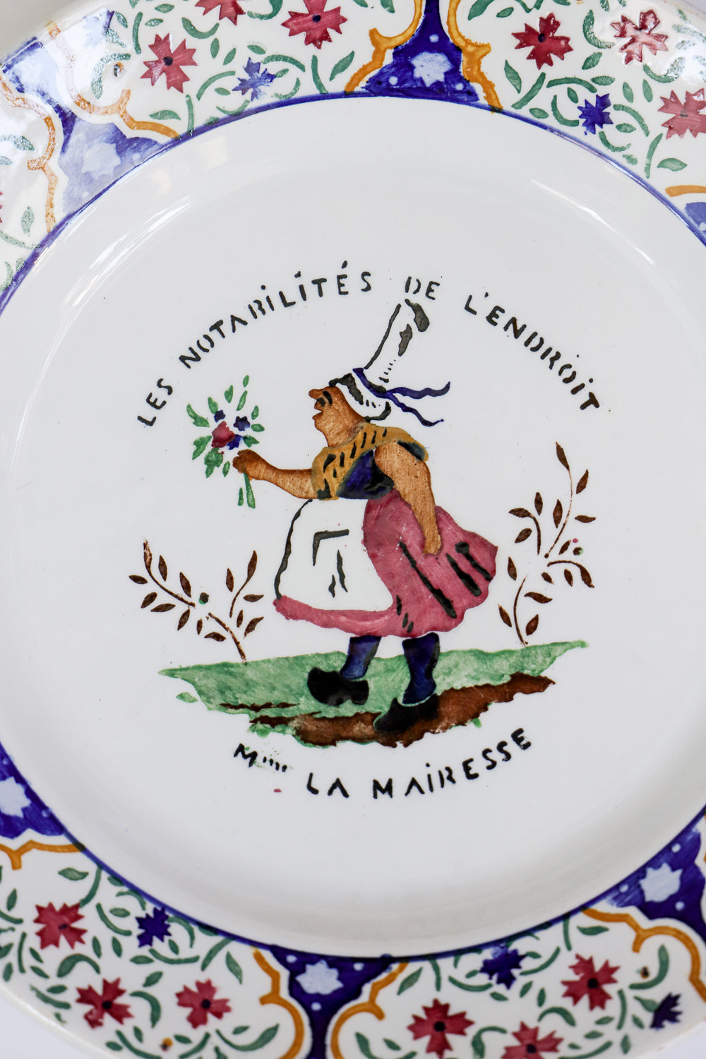 Close-up of a vintage Gien majolica ceramic plate with a hand-painted depictions of 'Madame La Mairesse' in a floral and colorful design