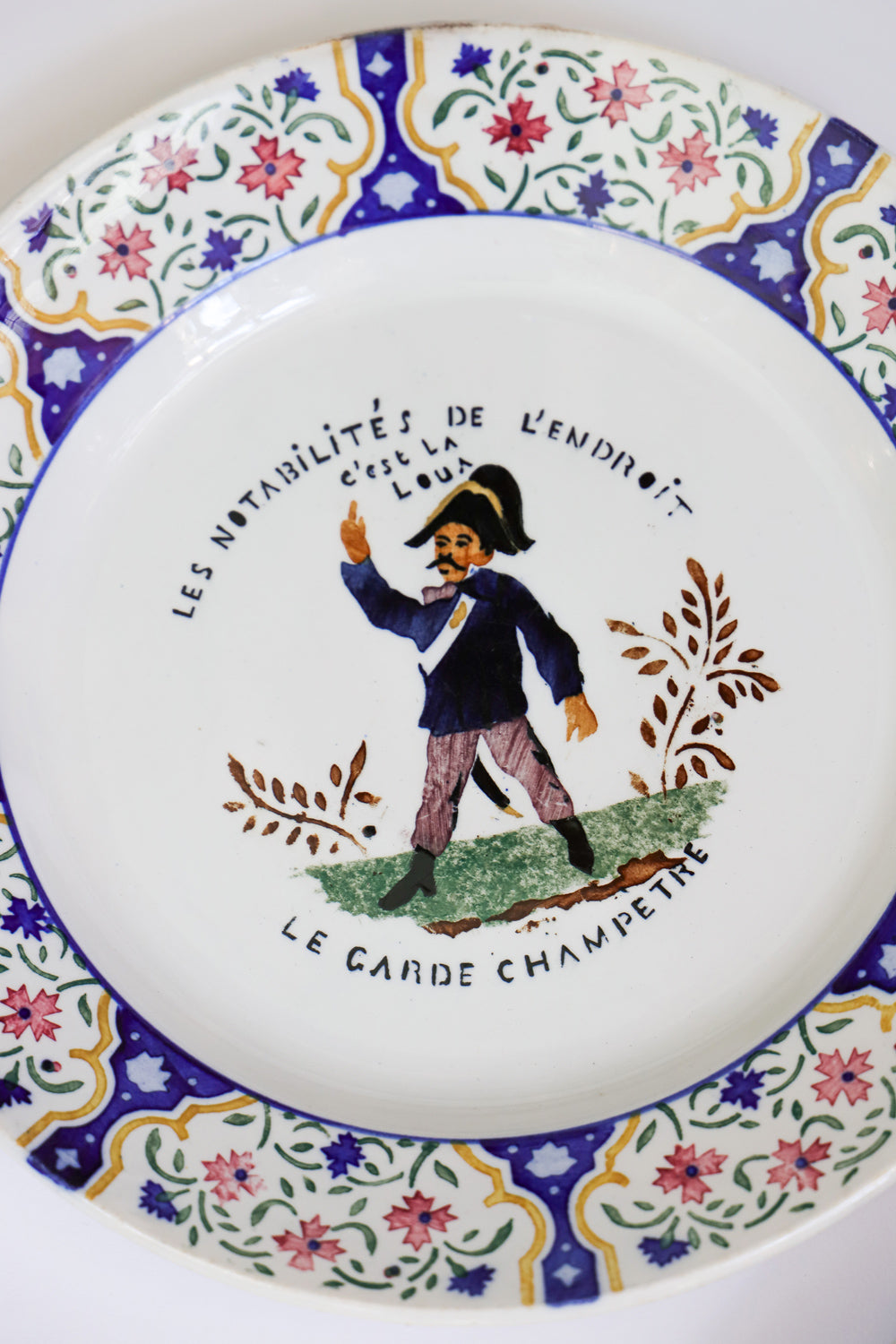 Close-up of a vintage Gien majolica ceramic plate with a hand-painted depiction of a 'Garde Champére' in a floral and colorful design