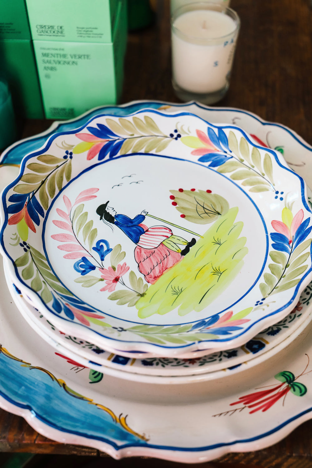 Stack of colorful ceramic plates topped with a vintage majolica plate featuring a hand-painted portrait of a man, scalloped edges, and floral motifs, available at Wildschut Antiques.