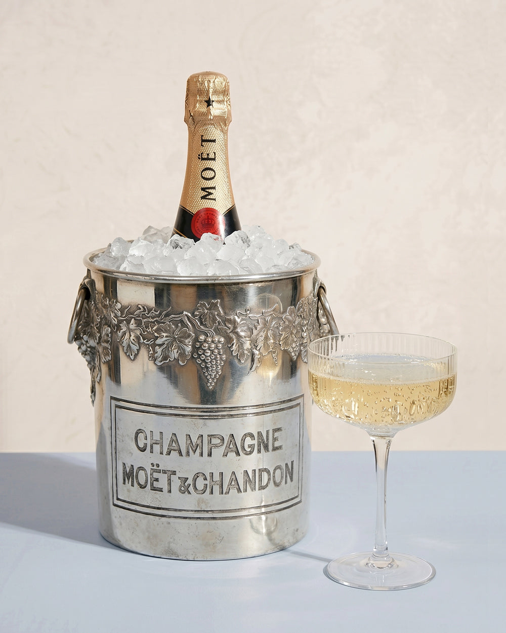 Moét & Chandon champagne bottle in a vintage silver plated ice bucket with Moét & Chandon branding and a glass of champagne on a light background. Available at Wildschut Antiques.
