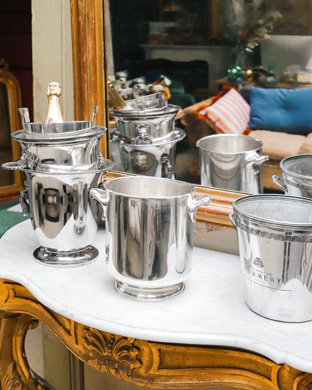 A curated collection of vintage silver-plated champagne and wine coolers in front of an antique mirror from Wildschut Antiques