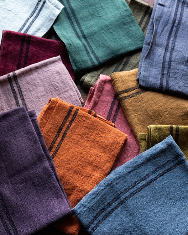 Collection of folded colorful linen towels in various patterns and colors. Linen country towels by Charvet Editions available via Wildschut Antiques.