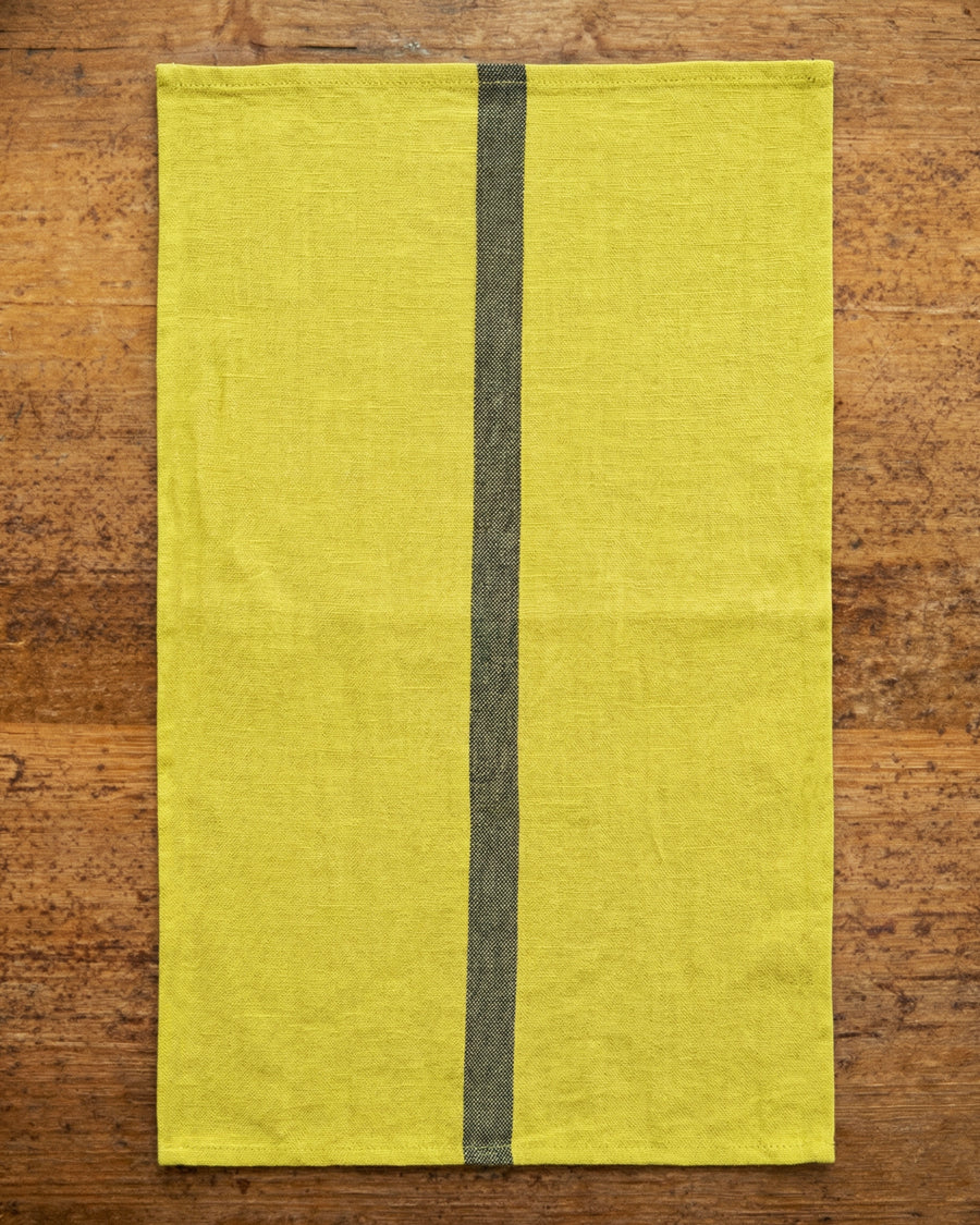 Lemon yellow linen towel with a dark stripe on a wooden surface, by Charvet Editions available via Wildschut Antiques.