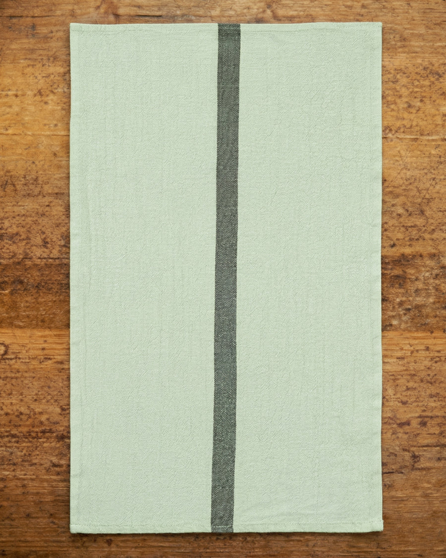Light green linen towel with a dark stripe on a wooden surface, by Charvet Editions available via Wildschut Antiques.
