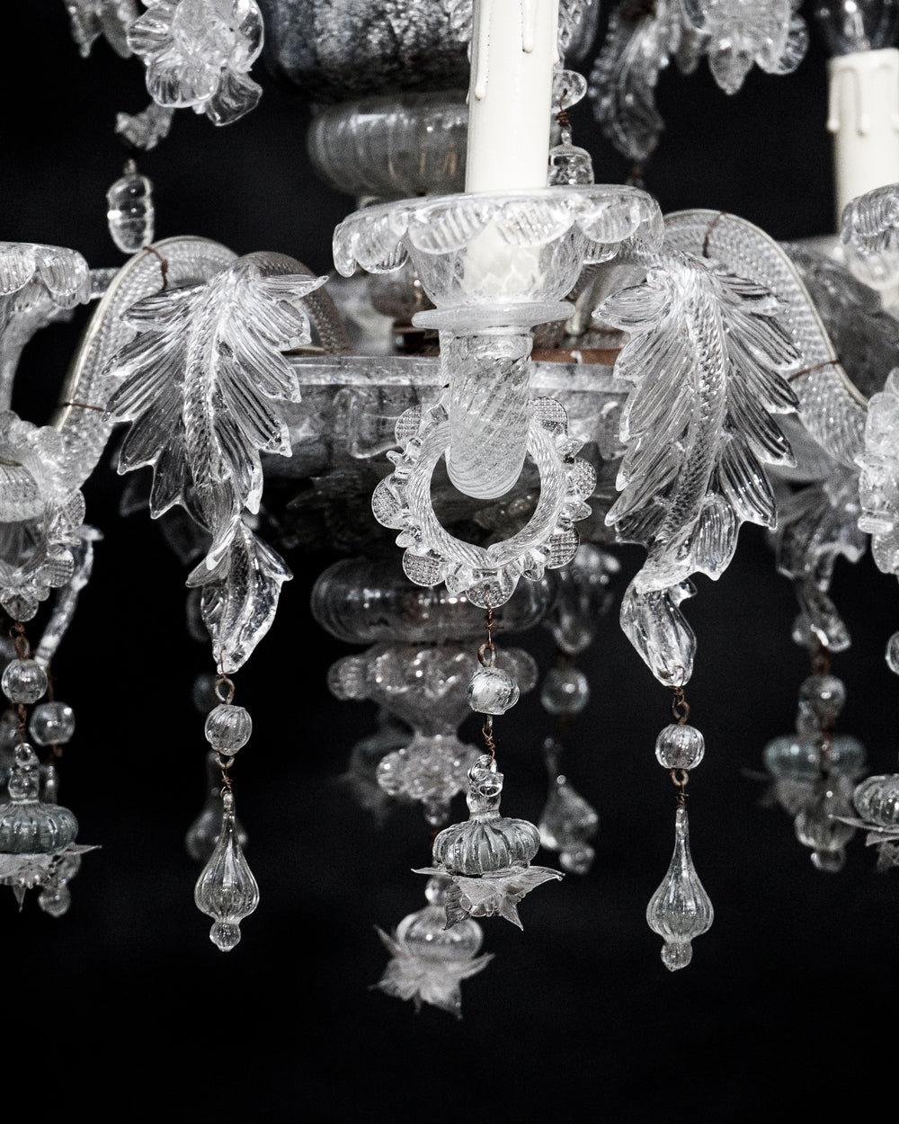 Close-up of a clear, hand-blown glass Venetian chandelier with six lights and intricate details, set against a black background
