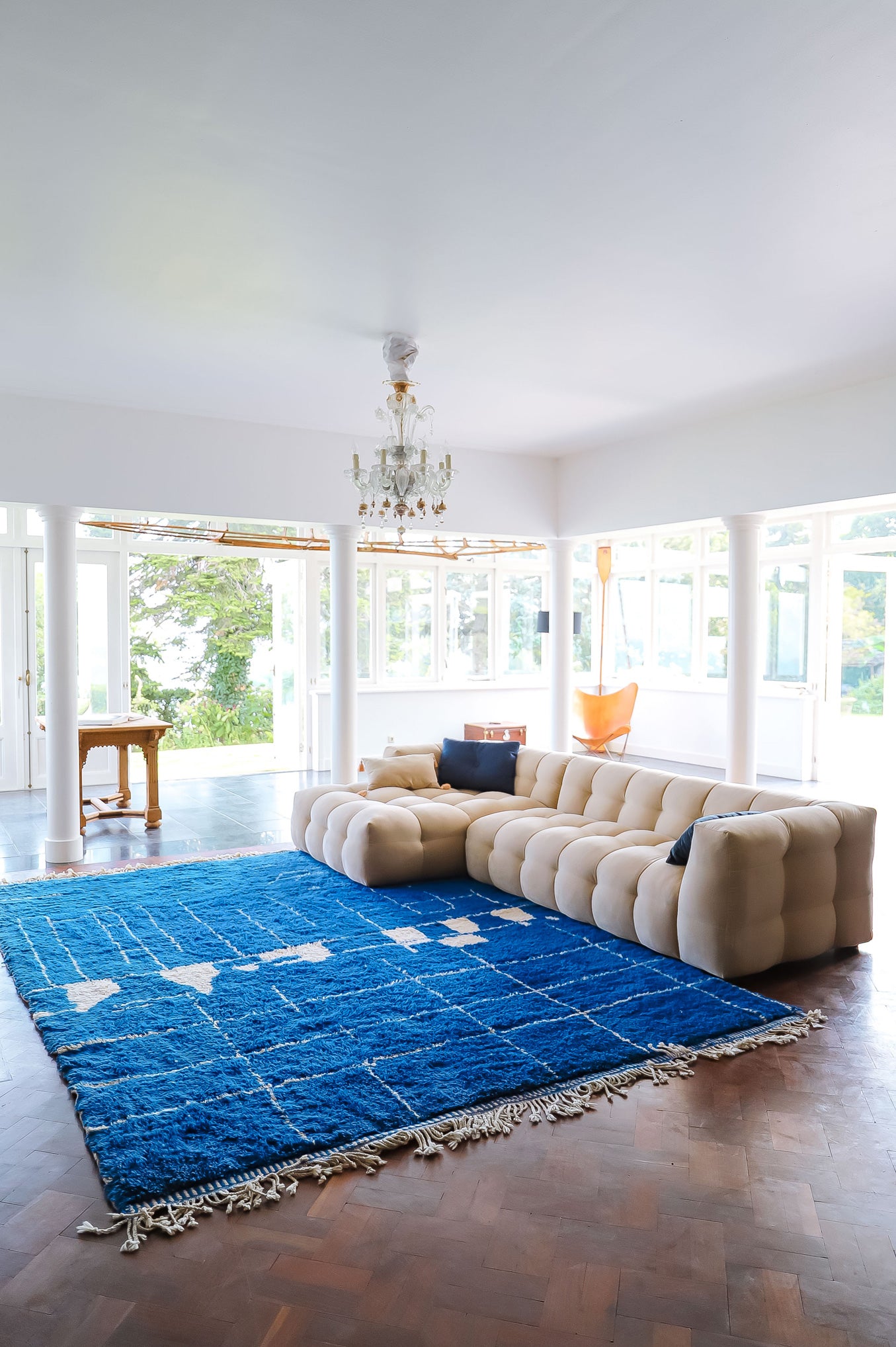 Spacious, light-filled room with a dark wooden floor and a soft cream-colored sofa. In front of the sofa lies a large vintage cobalt blue Moroccan rug, accented with asymmetrical white lines.