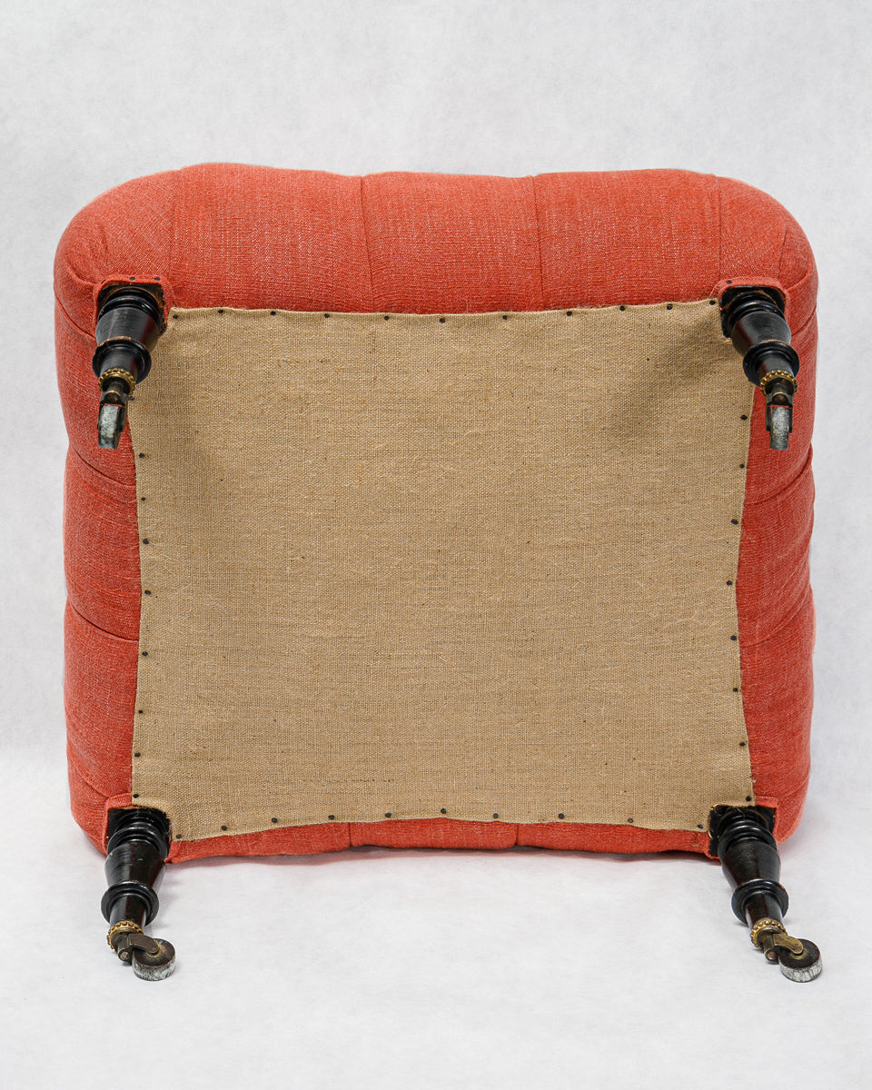Coral red cushioned stool with black wooden legs on a white background