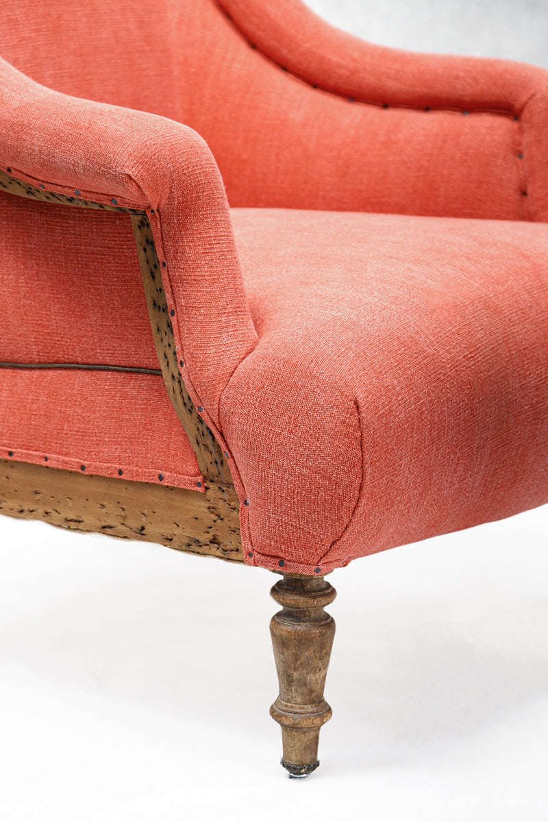 Close-up of a coral-colored antique French armchair with wooden legs on a white background.