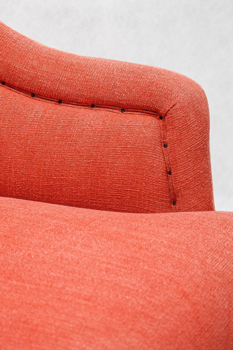Close-up of a coral red upholstered chair with a plain background.