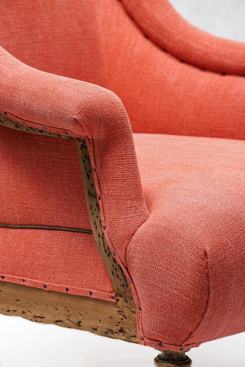 Close-up of a coral upholstered chair with wooden armrests on a white background