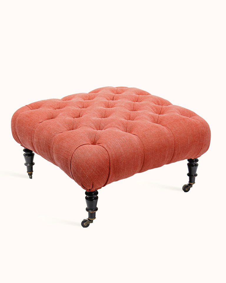 Coral tufted ottoman in Napoleon-III style with black legs on a white background - from Wildschut Antiques