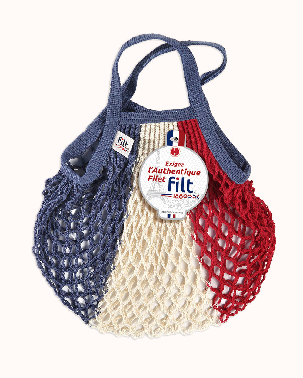 A reusable mesh shopping bag with blue, cream, and red vertical sections, featuring a blue handle and a round white Filt brand tag attached to the front. By Filt 1860, available at Wildschut Antiques & Decor.