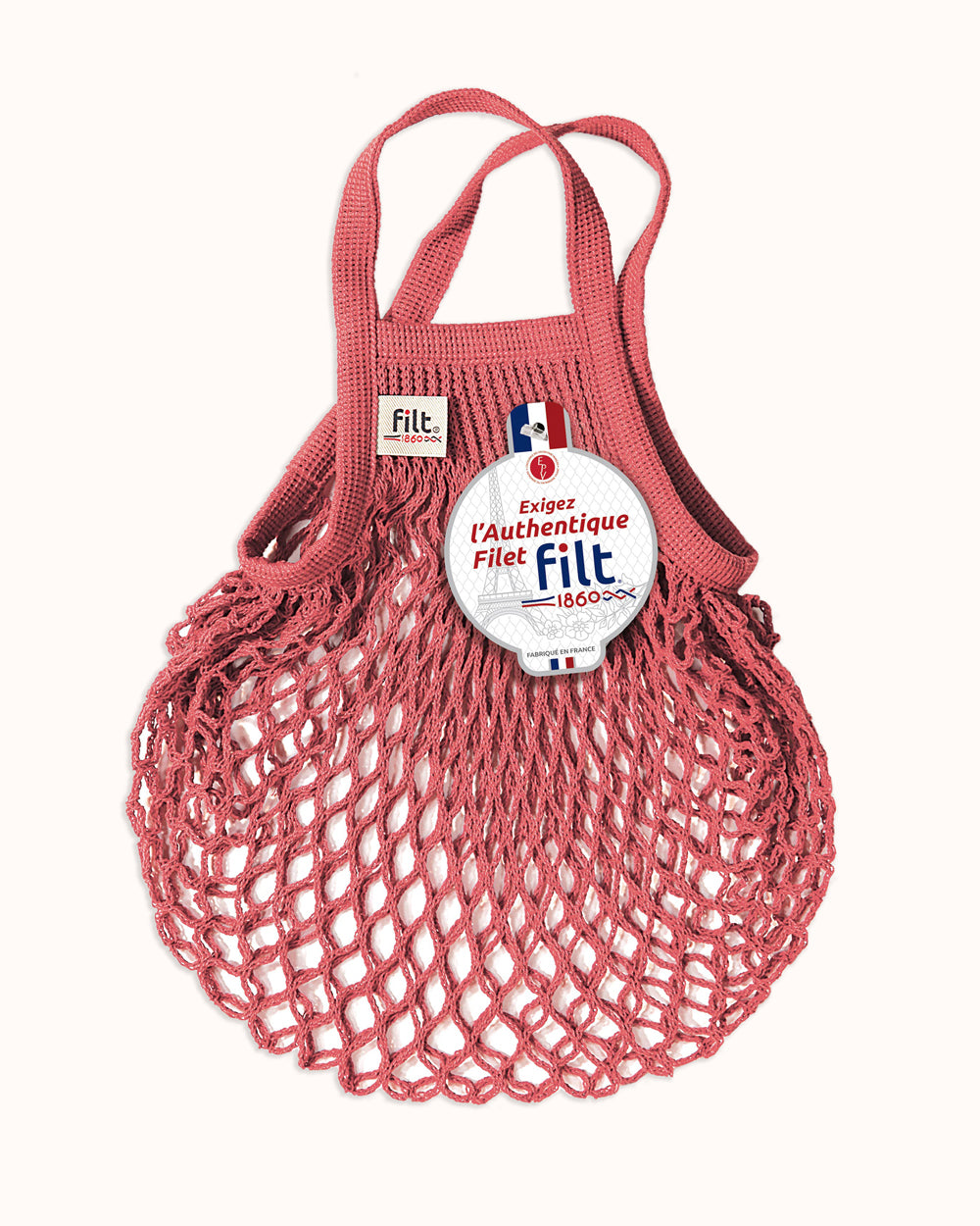 A coral red mesh net tote bag with double straps, featuring a circular white and blue Filt 1860 brand label on the front and a small Filt brand tag on the upper left side, set against a solid off-white background. By Filt 1860, available at Wildschut Antiques.