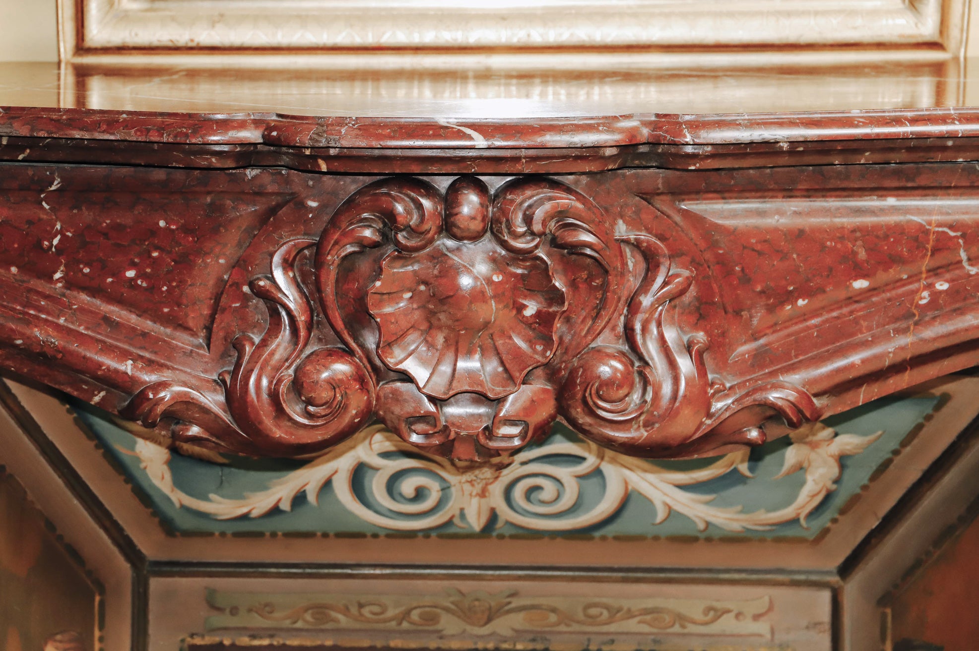 Close-up of a shell shape at the front of a grand antique French Rococo Louis XV fireplace mantel, crafted from richly veined red-brown marble.