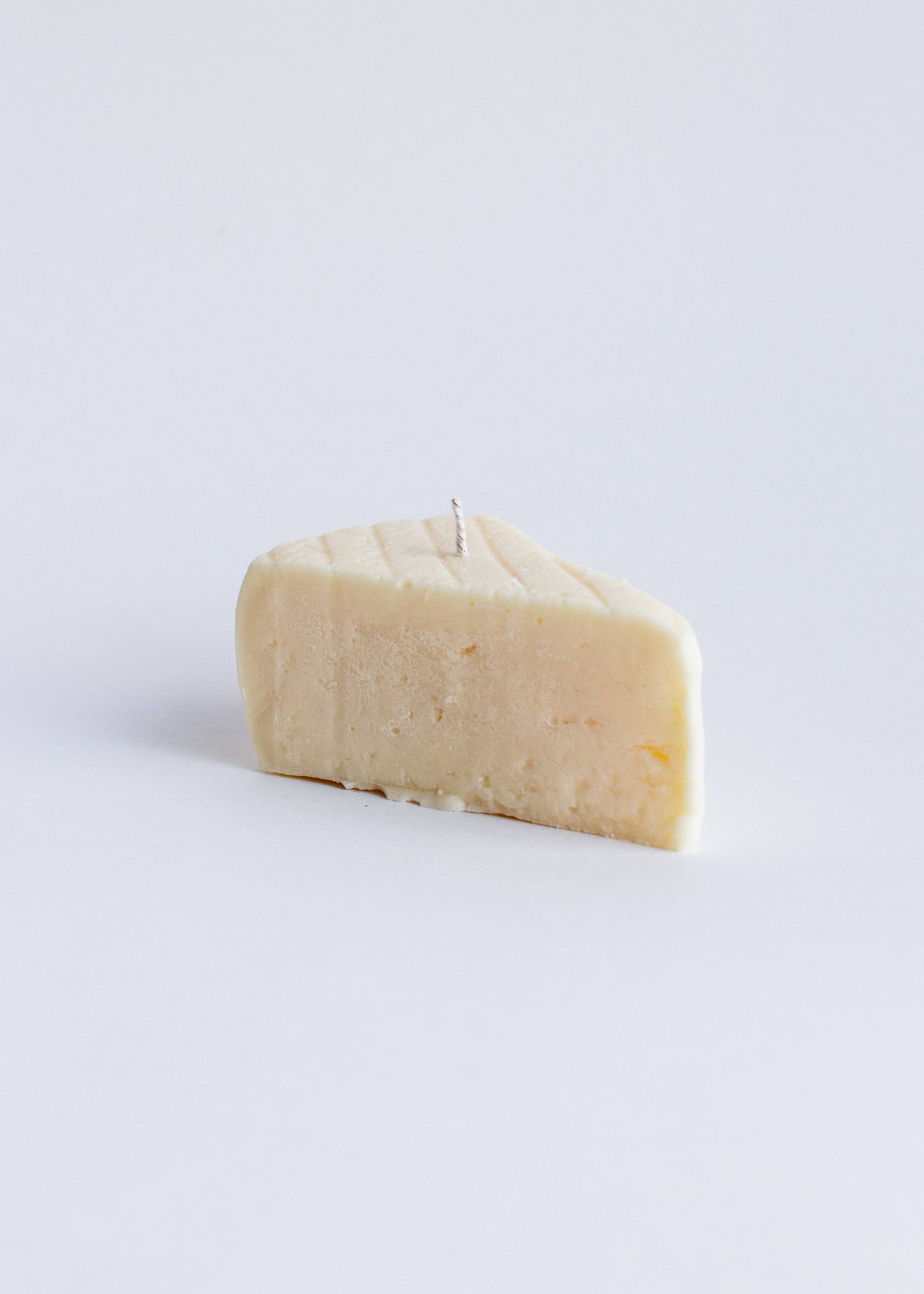Block of brie cheese on a light gray background. Fun fact: this is not a real piece of brie, it is a candle! Part of the Playful Food Candle Collection available via Wildschut Antiques Concept Store
