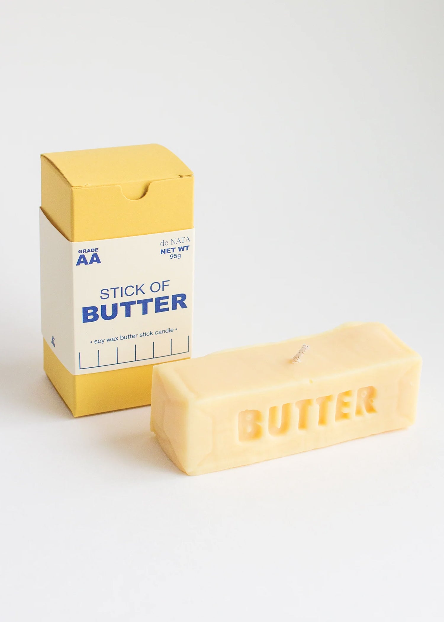 Candle in the shape of a stick of butter with packaging on a white background. Part of the Playful Food Candle Collection available via Wildschut Antiques Concept Store.