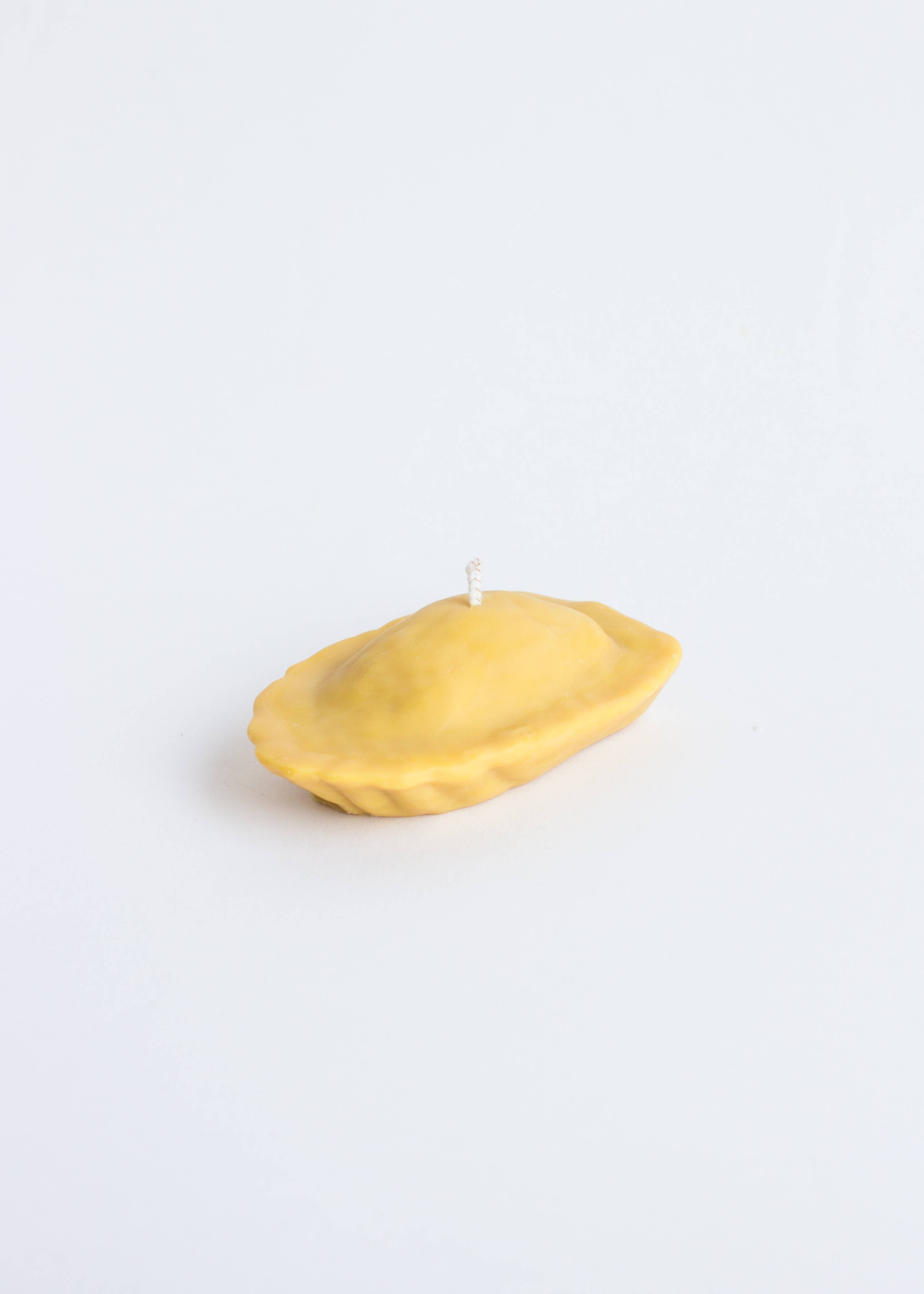 Beeswax candle shaped like a small French Madeleine cake on a white background