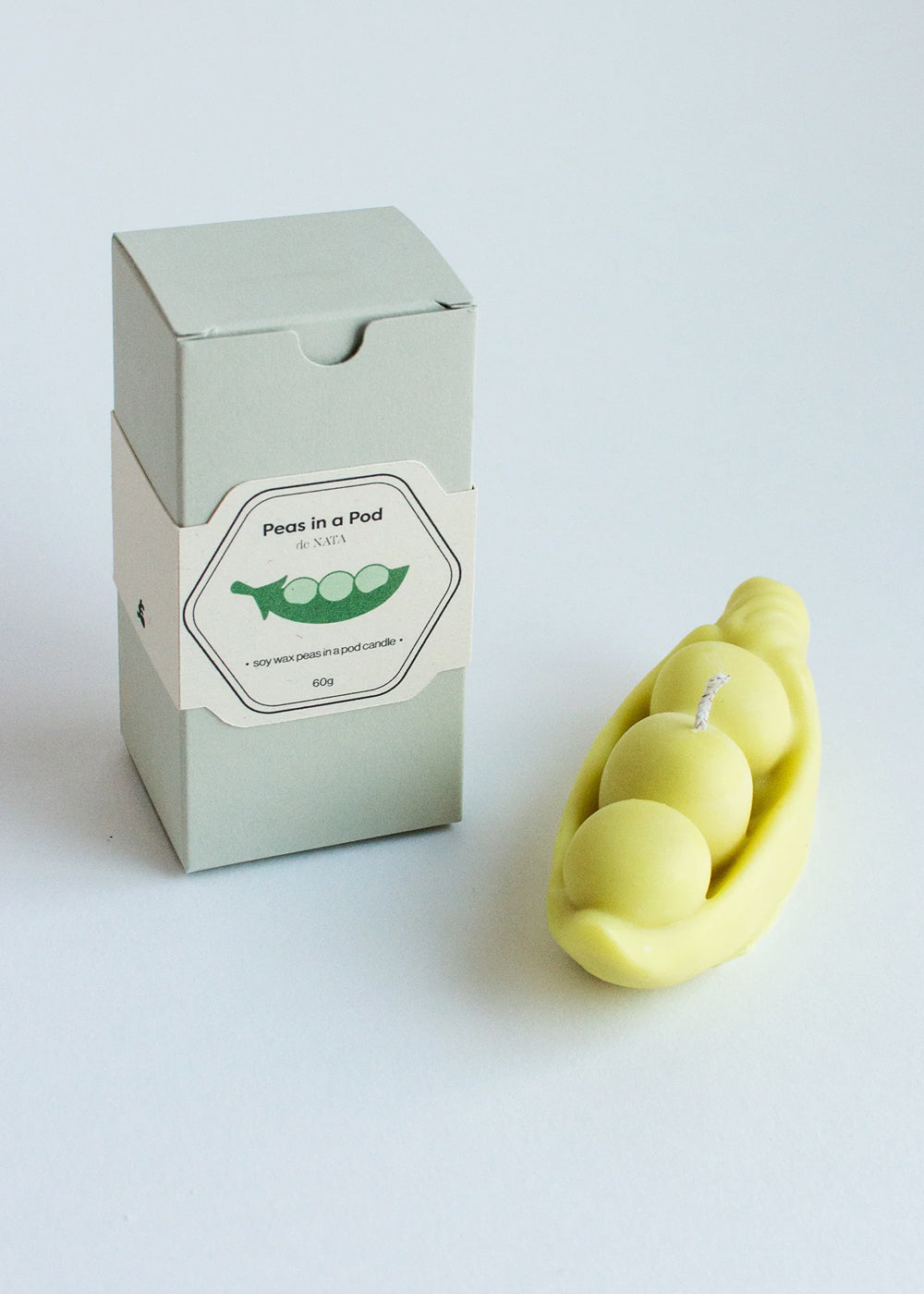 Candle in the shape of peas in a pod. next to its packaging. Part of the Playful Food Candle Collection available via Wildschut Antiques Concept Store.