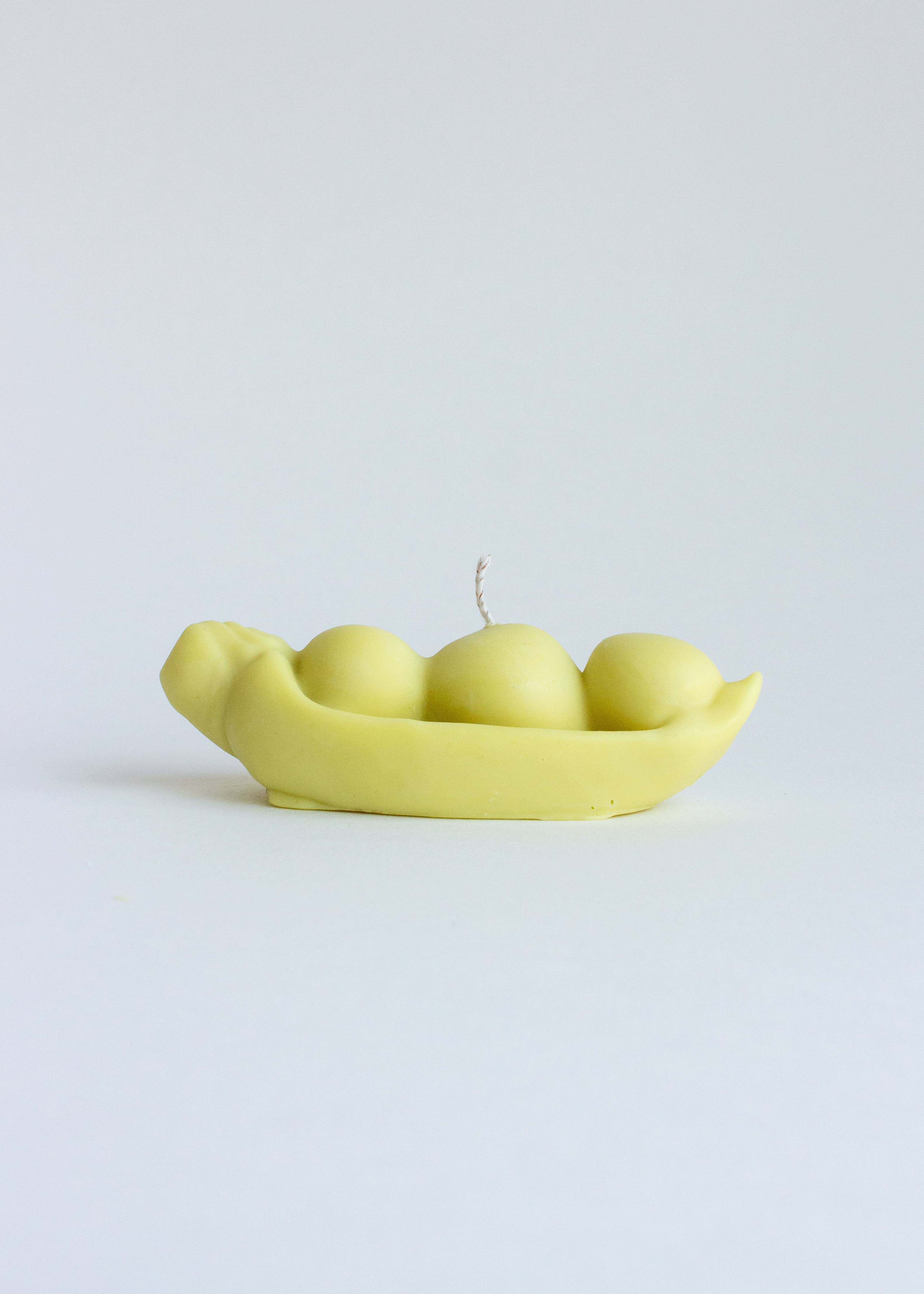 Light green candle shaped like a pod with three peas on a white background. Part of the Playful Food Candle Collection available via Wildschut Antiques Concept Store.