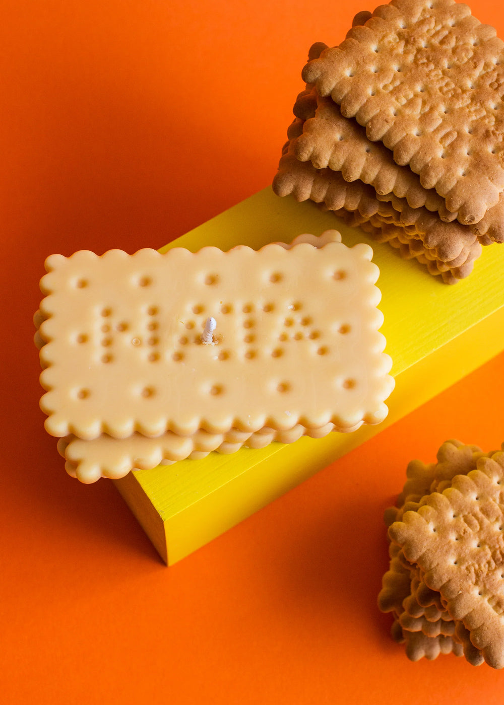 White biscuit-shaped candle on a yellow stand with brown cookies on an orange background