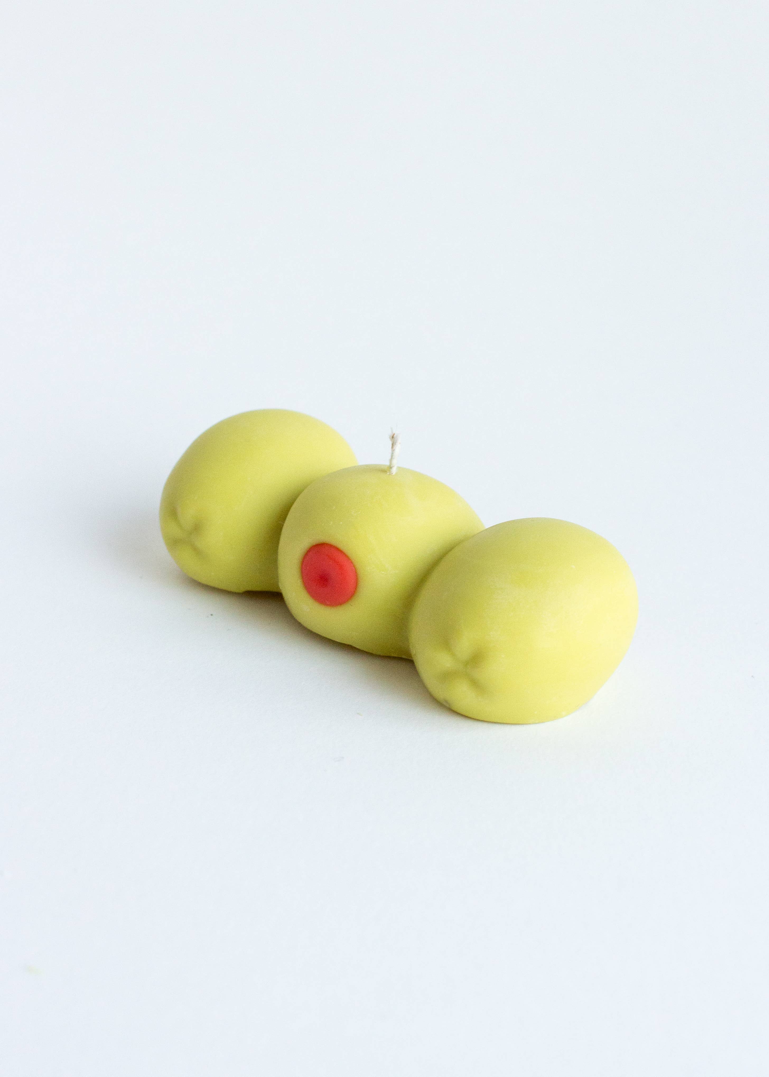 Candle in the shape of three green olives with a red center on a white background