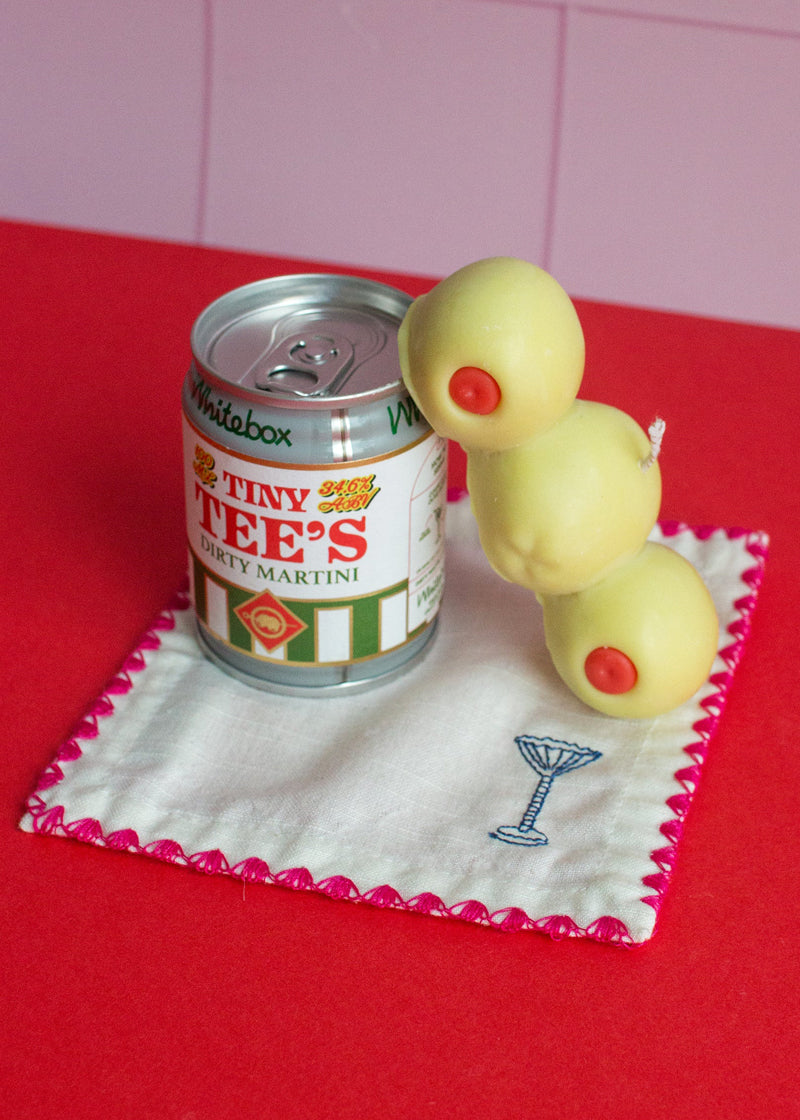 Miniature can of Tiny Tee's Dry Martini with olives-candle on a red surface