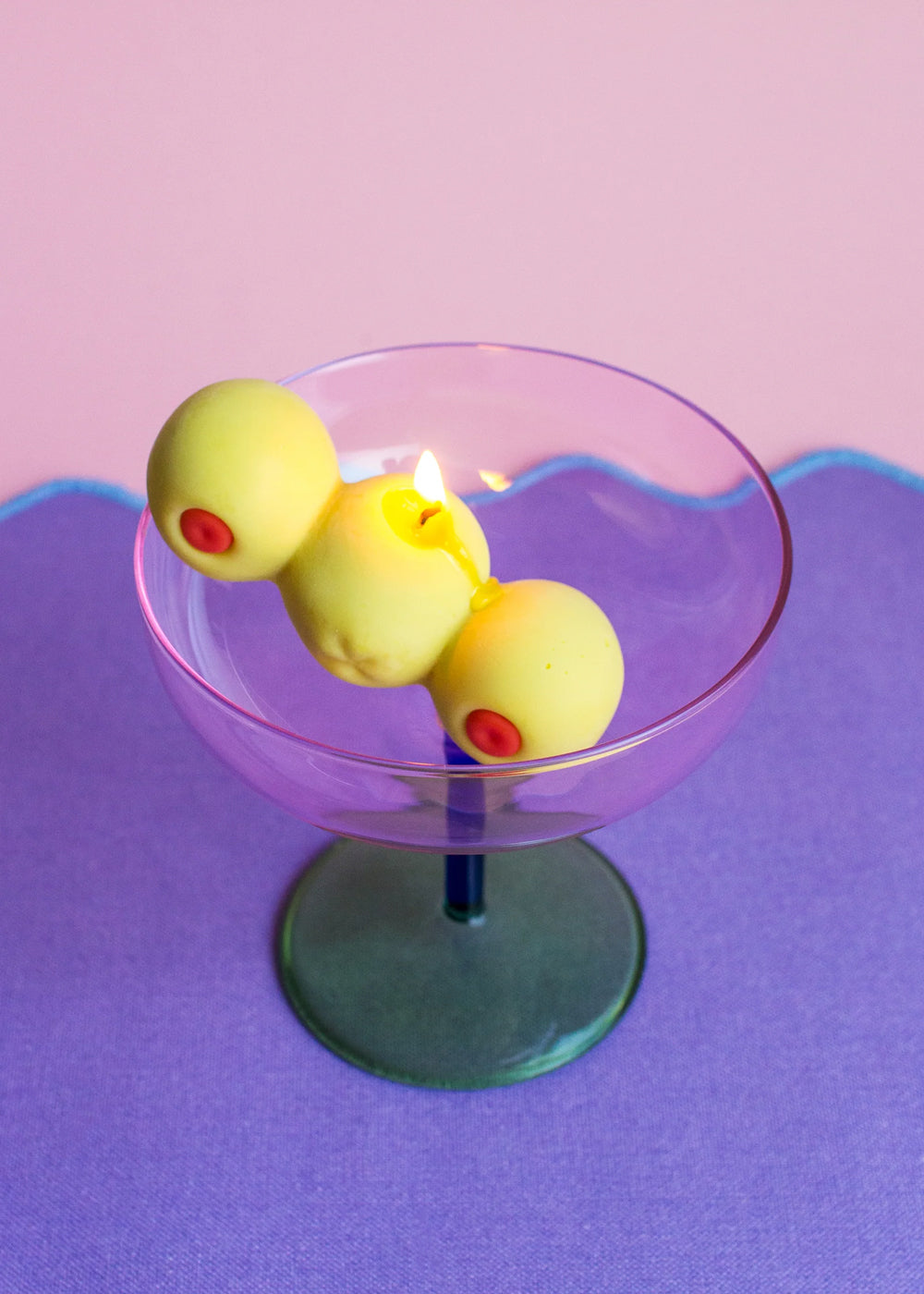Cocktail glass with a candle in the shape of three light green olives on a purple background