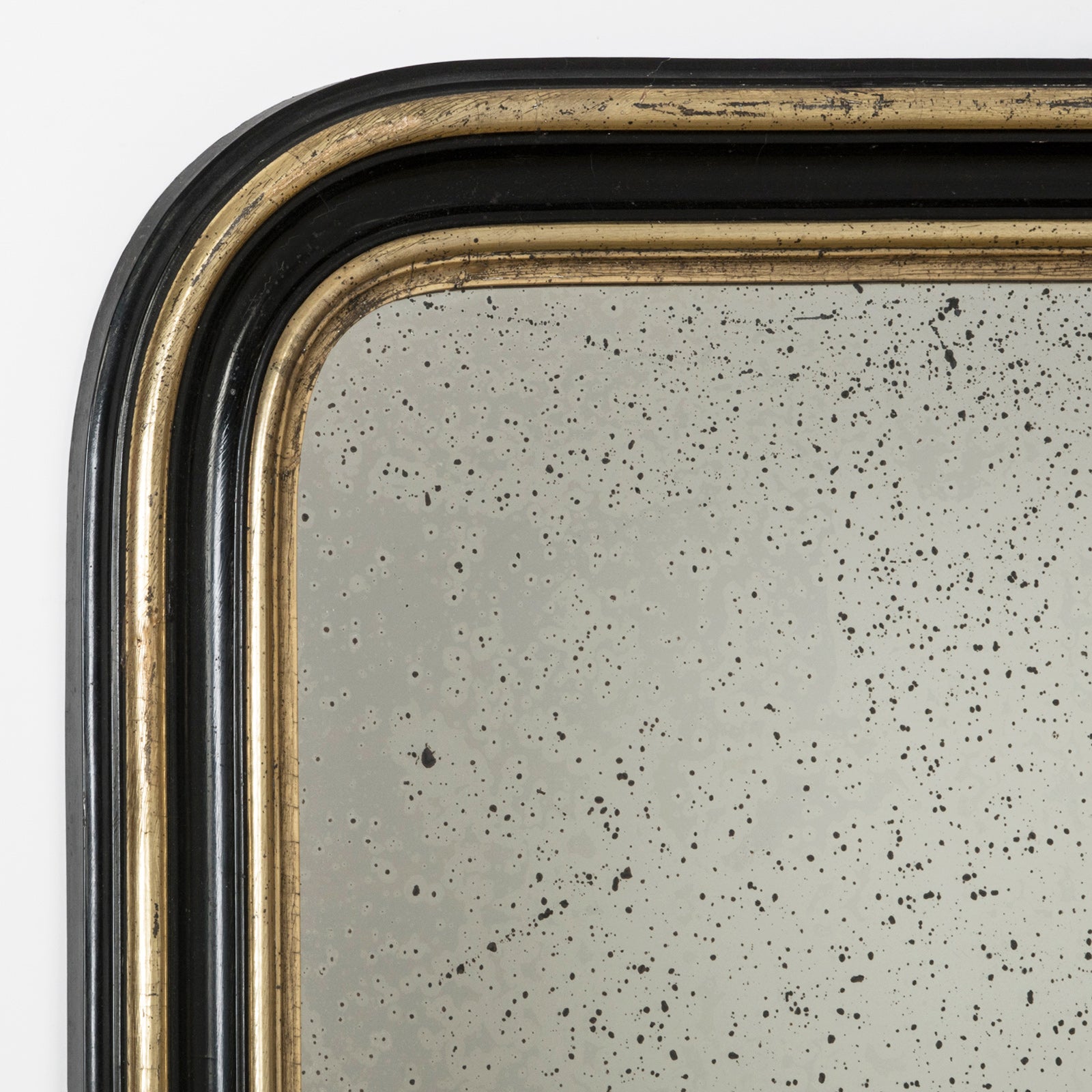 Close-up of the top part of a an elegant antique black and gold frame mirror with visible signs of foxing on the mirror surface, available at Wildschut Antiques