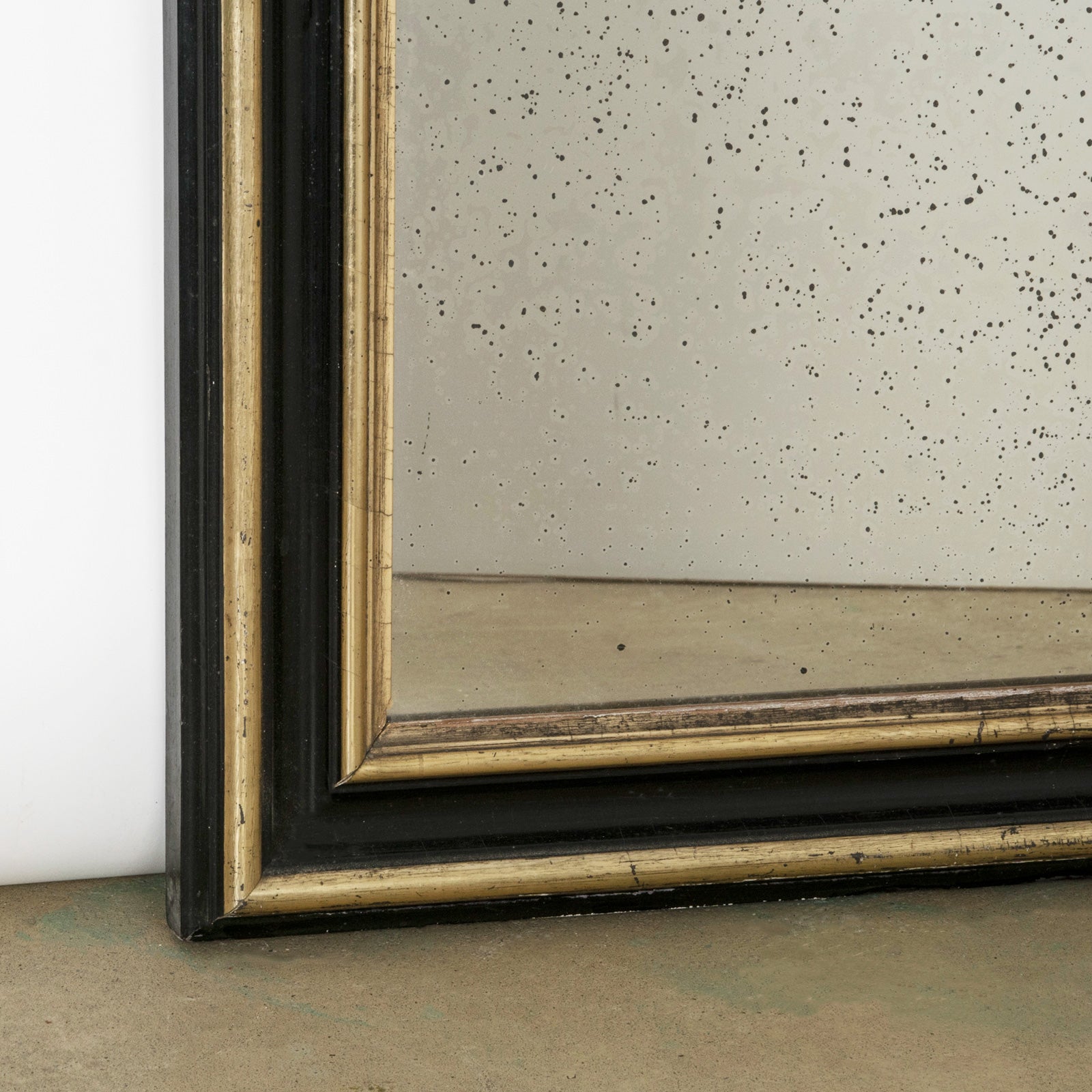 Close-up of the lower part of a an elegant antique black and gold frame mirror with visible signs of foxing on the mirror surface