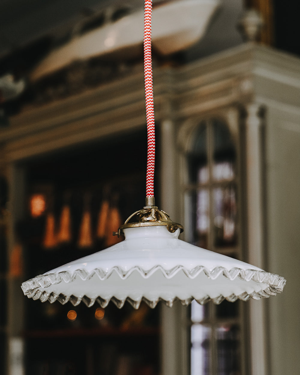 A vintage French white glass frilled coolie pendant light with red and white electrical wiring, hanging from the ceiling and available at Wildschut Antiques