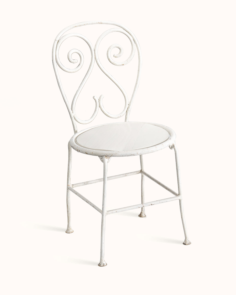 Vintage French white metal garden chair with ornate decorative backrest, displayed on a white background, sideview.