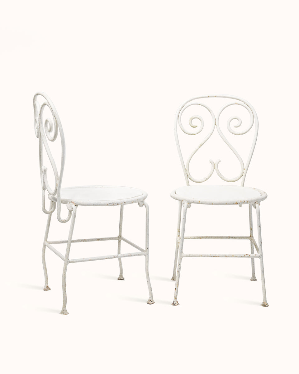 Two white metal vintage French garden or cafe chairs with decorative backrests on a plain background - from Wildschut Antiques