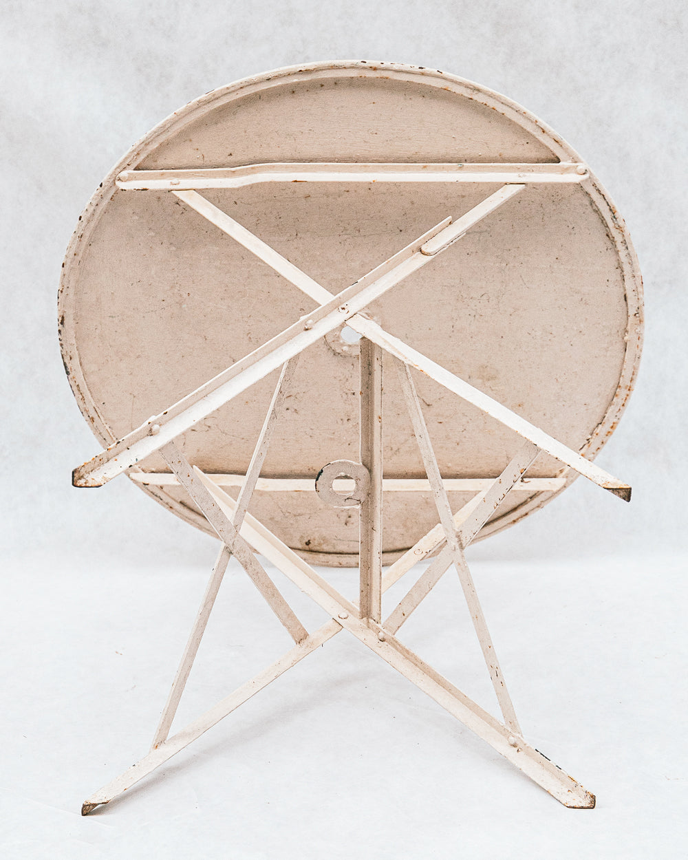 Bottom view of a vintage early 20th-century French folding metal round garden table with a patinated iron frame set against a white background.