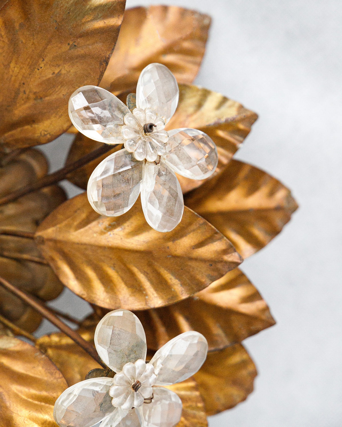 Close-up of a decorative wall or ceiling lamp with gold leaves and white flowers on a light background