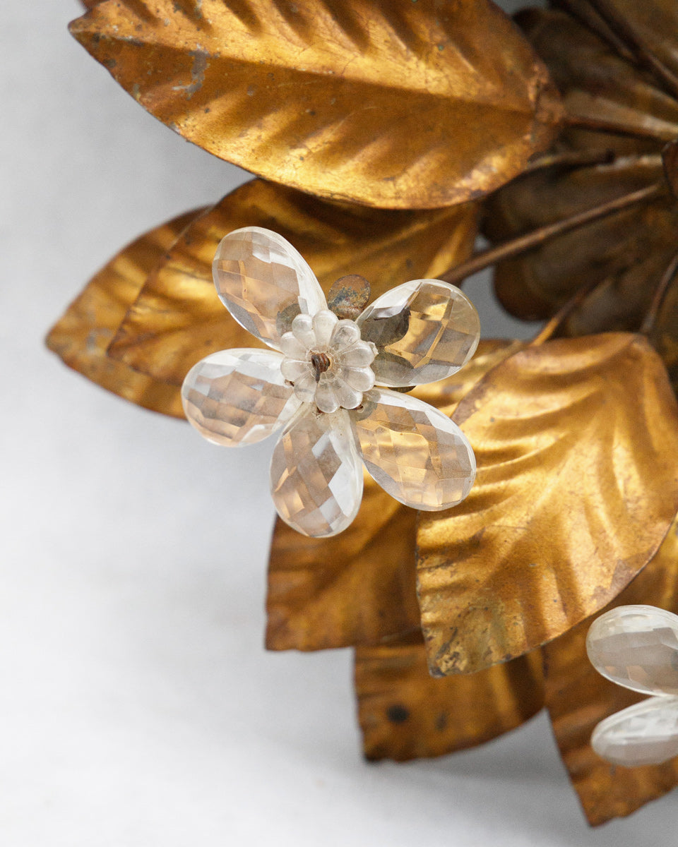 Close-up of a decorative wall or ceiling lamp with gold leaves and white flowers on a light background
