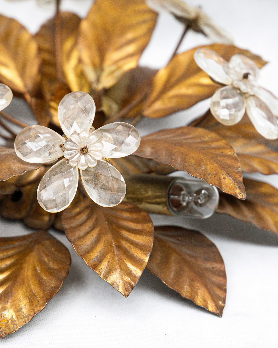 Decorative vintage French wall sconce with gold leaves and white glass flowers on a white background