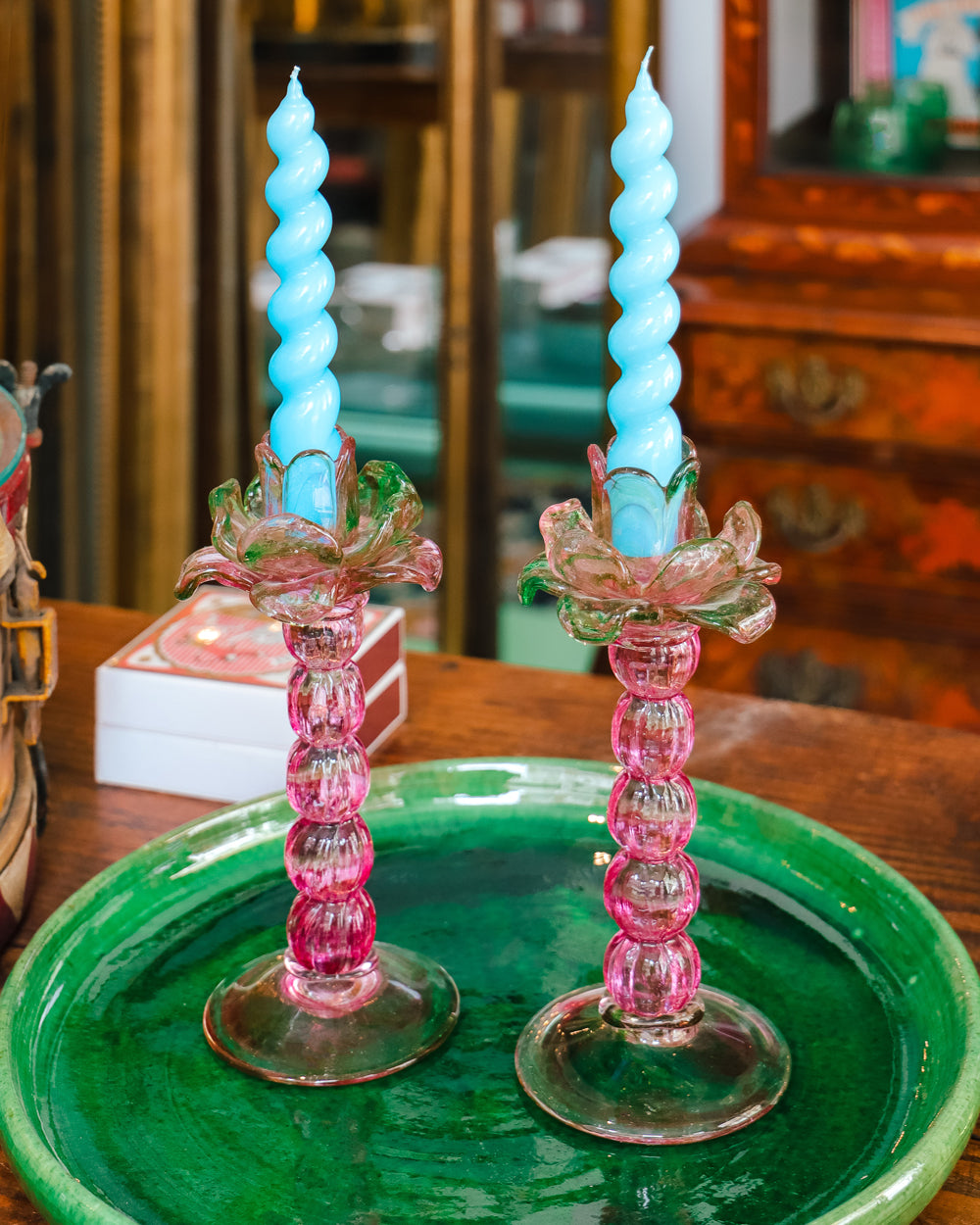 A pair of vintage Murano glass palm tree candle holders in green and pink colors with bright blue swirl candles on a emerald green platter in the store of Wildschut Antiques