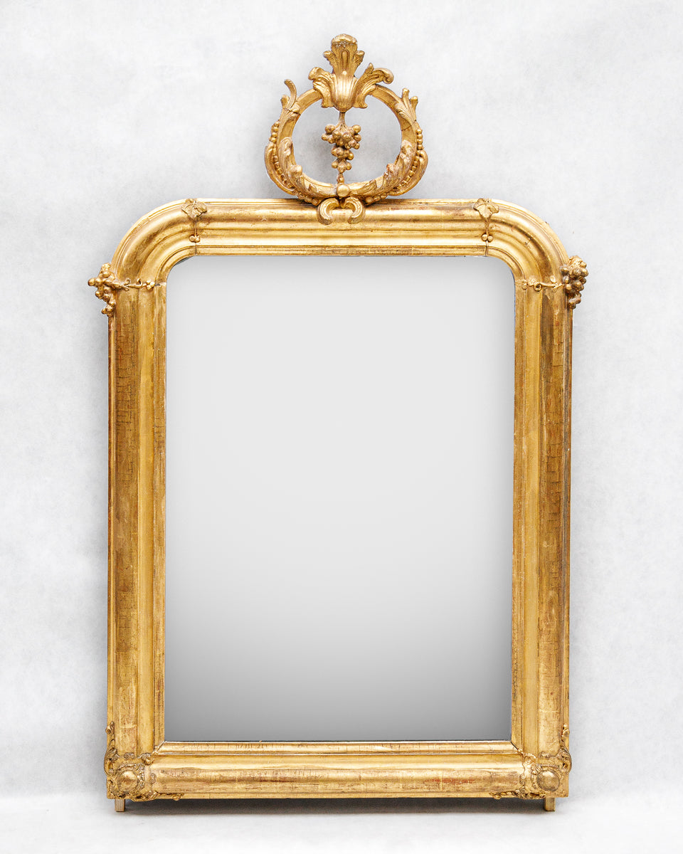 Decorative antique gold-framed mirror with an elaborate grapevine crest on a white background