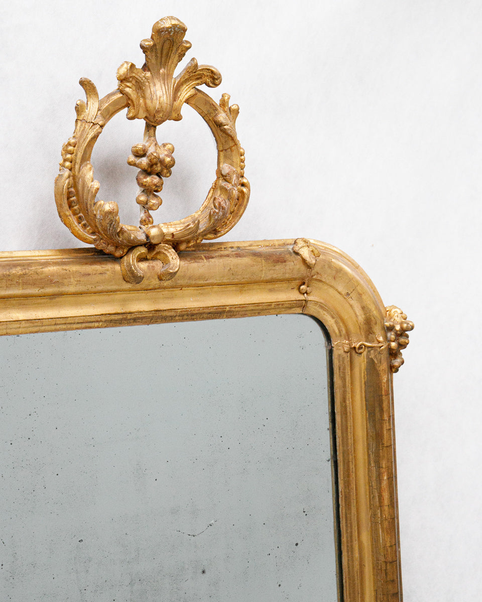 Gold-framed antique French mirror with decorative top on a white background from Wildschut Antiques