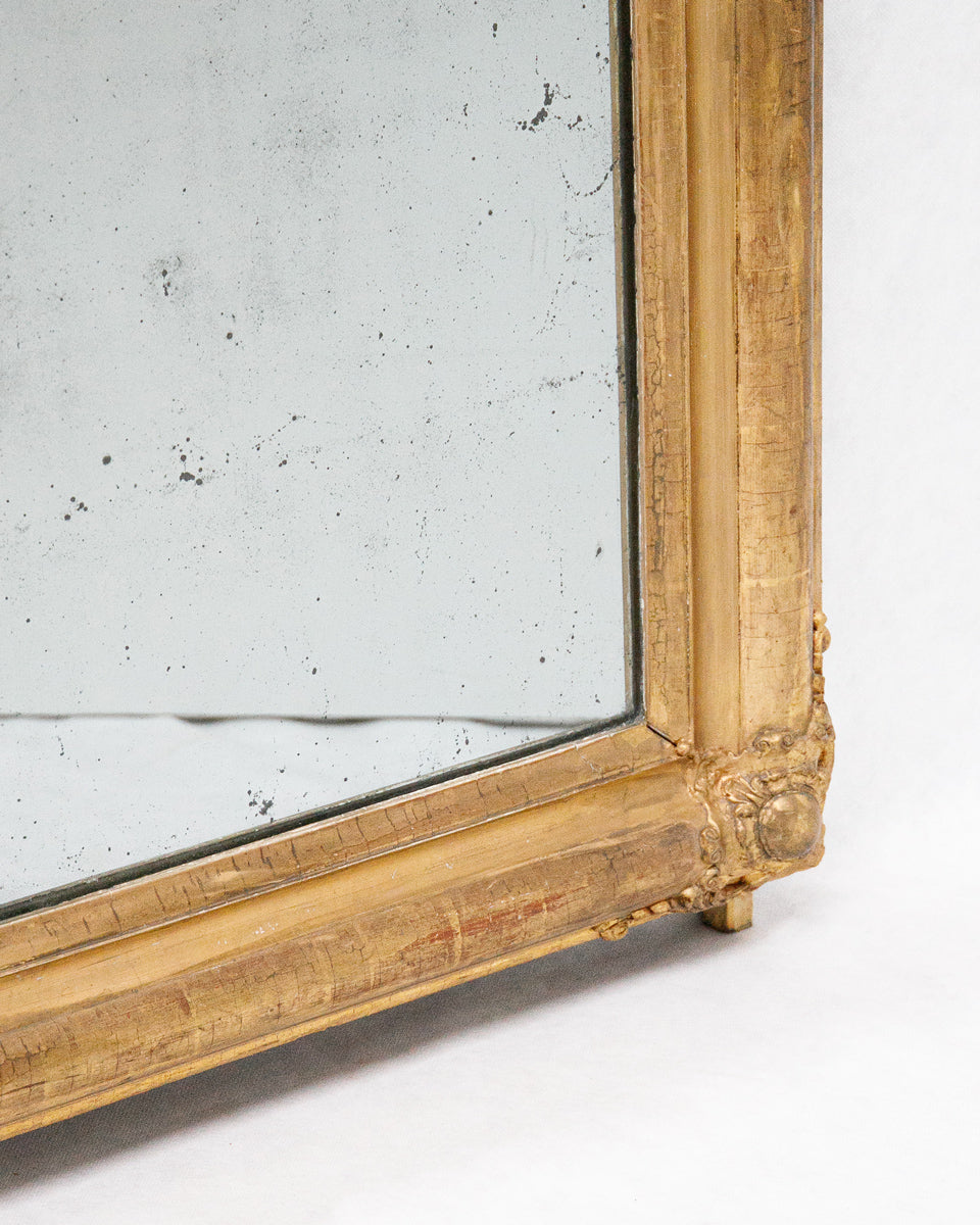 Close-up of a corner of an antique French gold-framed mirror with foxed glass on a white wall