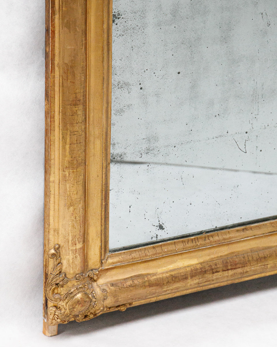 Close-up of a corner of an antique French gold-framed mirror with foxed glass on a white wall