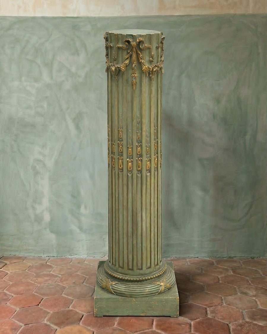 Decorative antique French green classic column against a textured green wall with a brick floor, available via Wildschut Antiques.