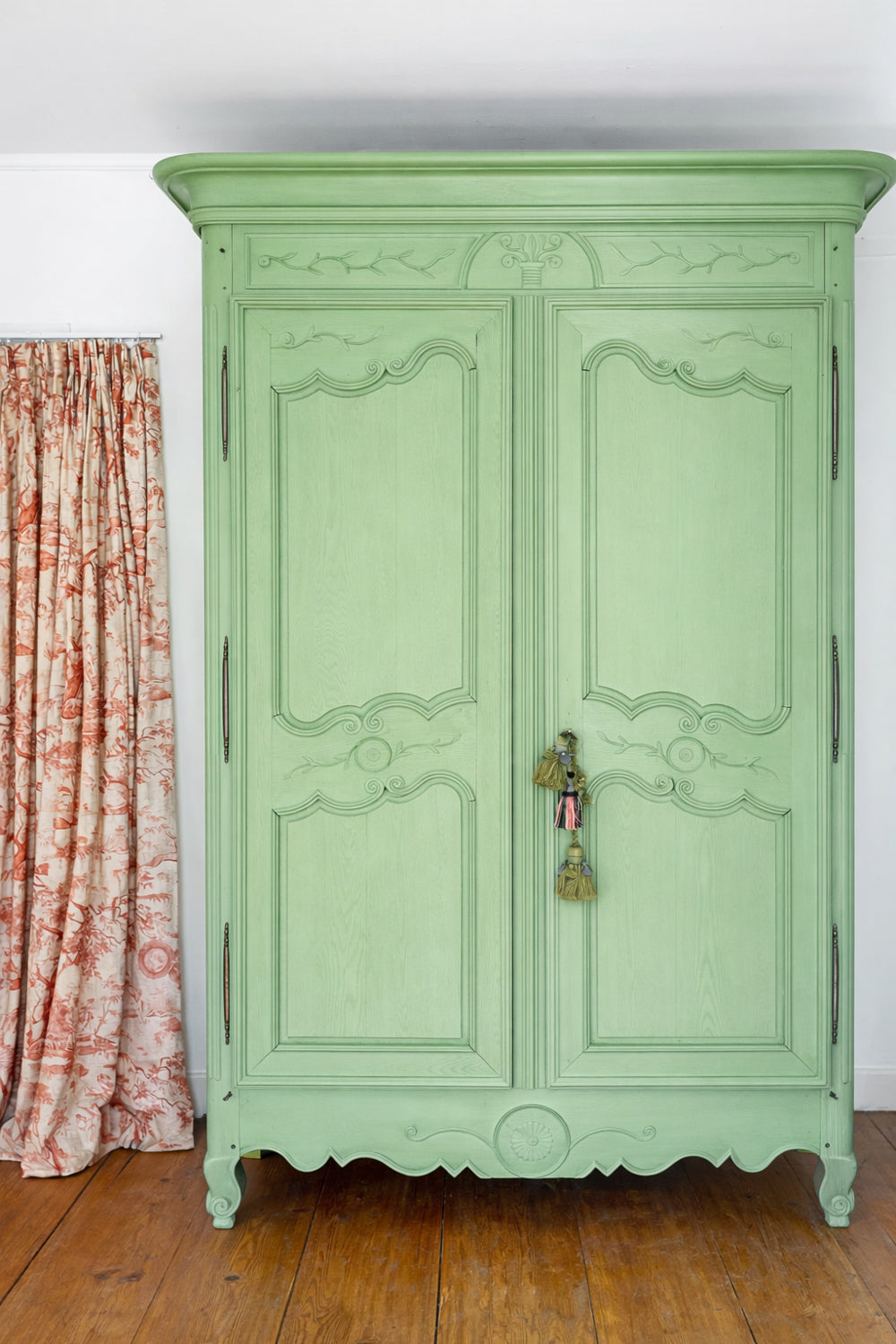 19th-century green painted French marriage armoire with carved foliage motifs on a rustic wooden floor. Available via Wildschut Antiques