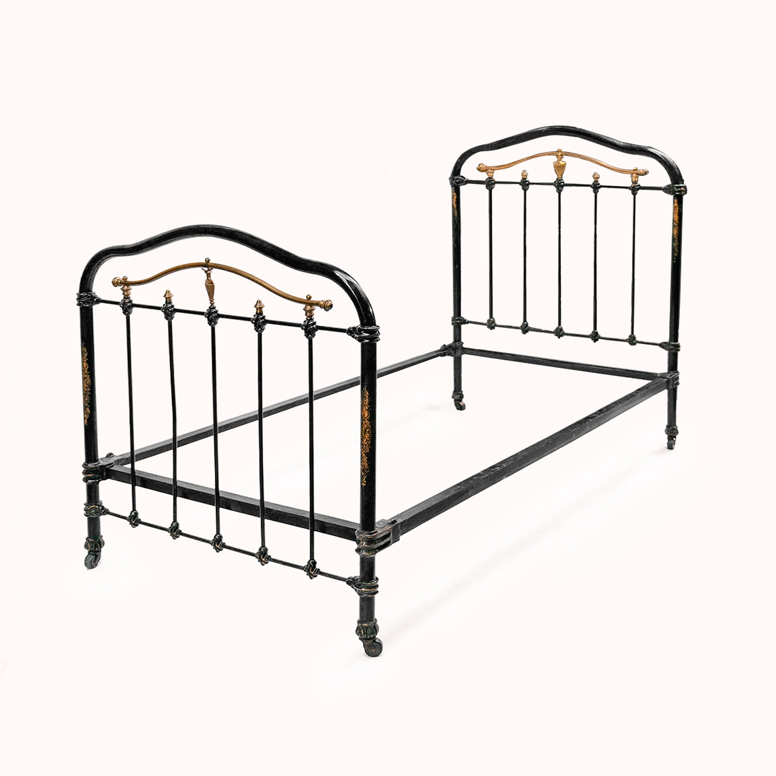 Antique cast iron single bed with black and gold finish, solid frame with intricate designs, small wheels on legs, no mattresses or slats included, available at Wildschut Antiques