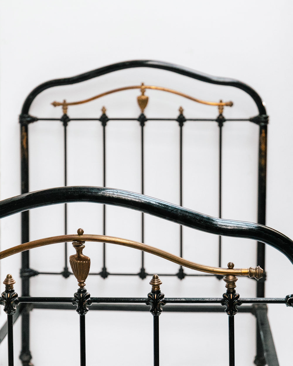 Close-up of an antique cast iron single bed with black and gold finish, solid frame with intricate designs, small wheels on legs, no mattresses or slats included