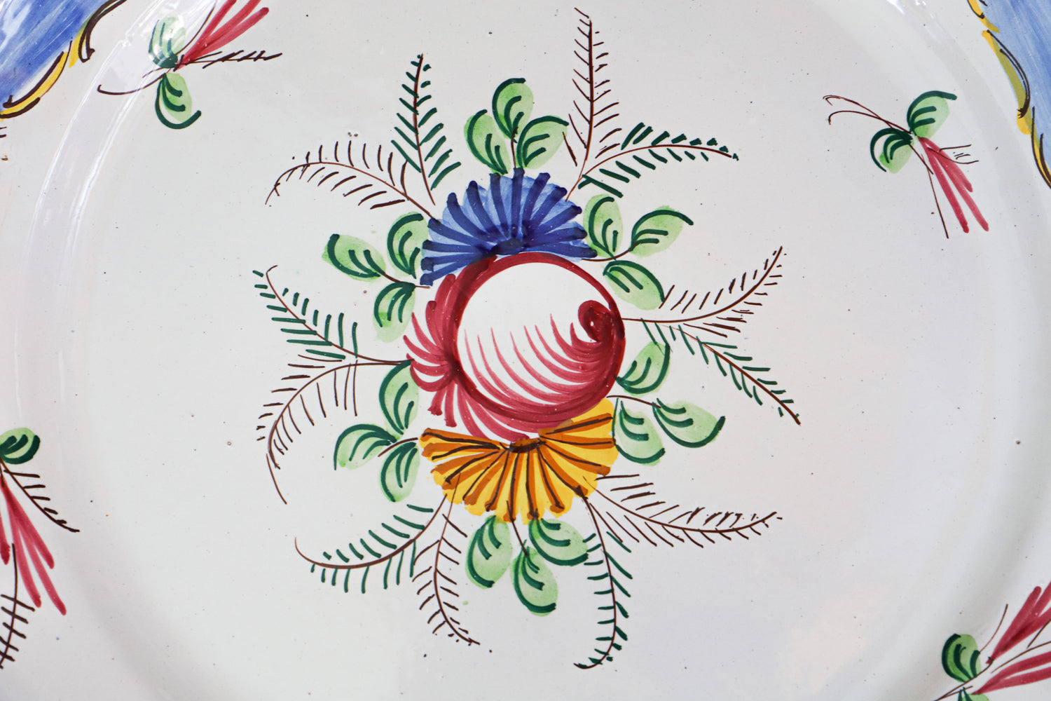 Close-up of a large vintage hand-painted Italian ceramic plate with a floral design, predominantly white with blue and yellow accents along the rim