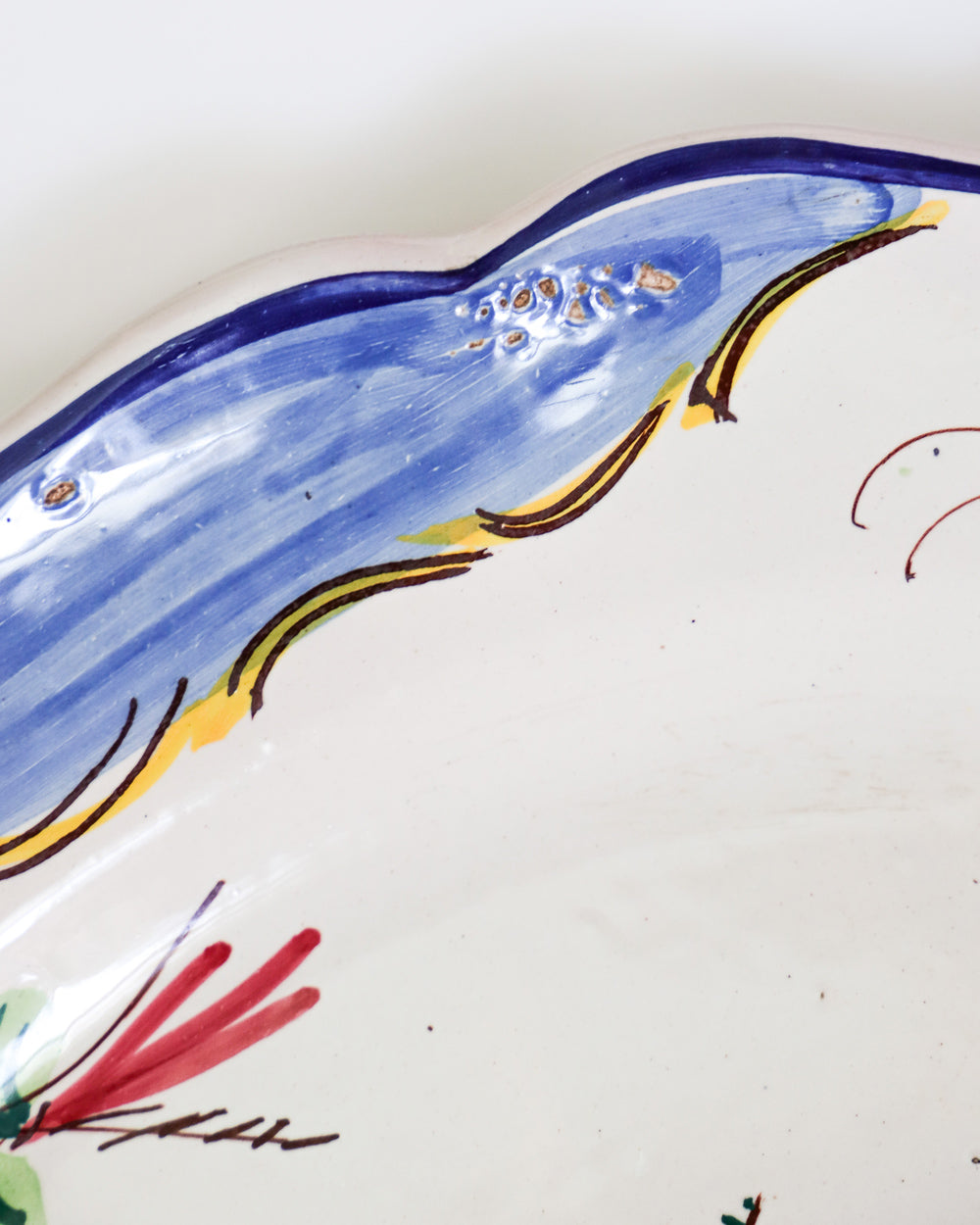 Close-up of a large vintage hand-painted Italian ceramic plate with a floral design, predominantly white with blue and yellow accents along the rim
