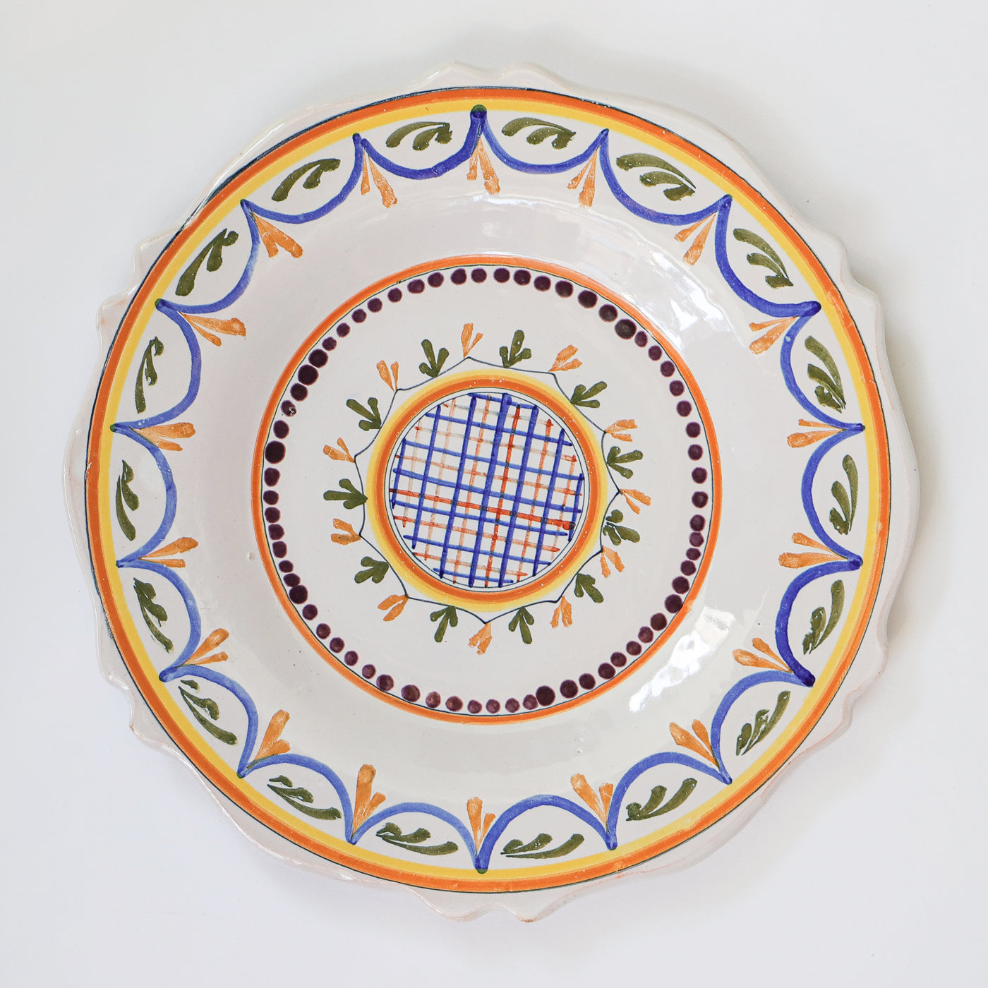 A small, vintage, hand-painted majolica ceramic plate with a geometric pattern, featuring swirls and foliate motifs in a combination of blue, green, and orange colors on a white background