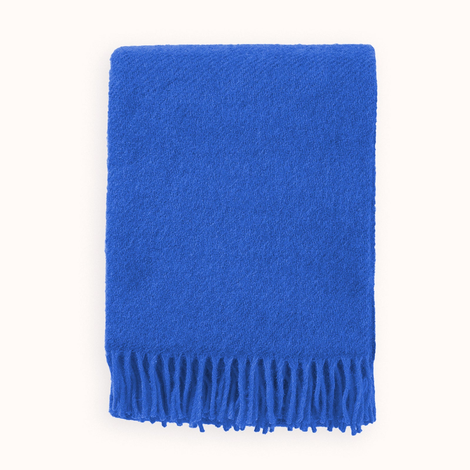 Neatly folded cobalt blue wool blanket with fringes on a white background, by Klippan 1879, available at Wildschut Antiques.